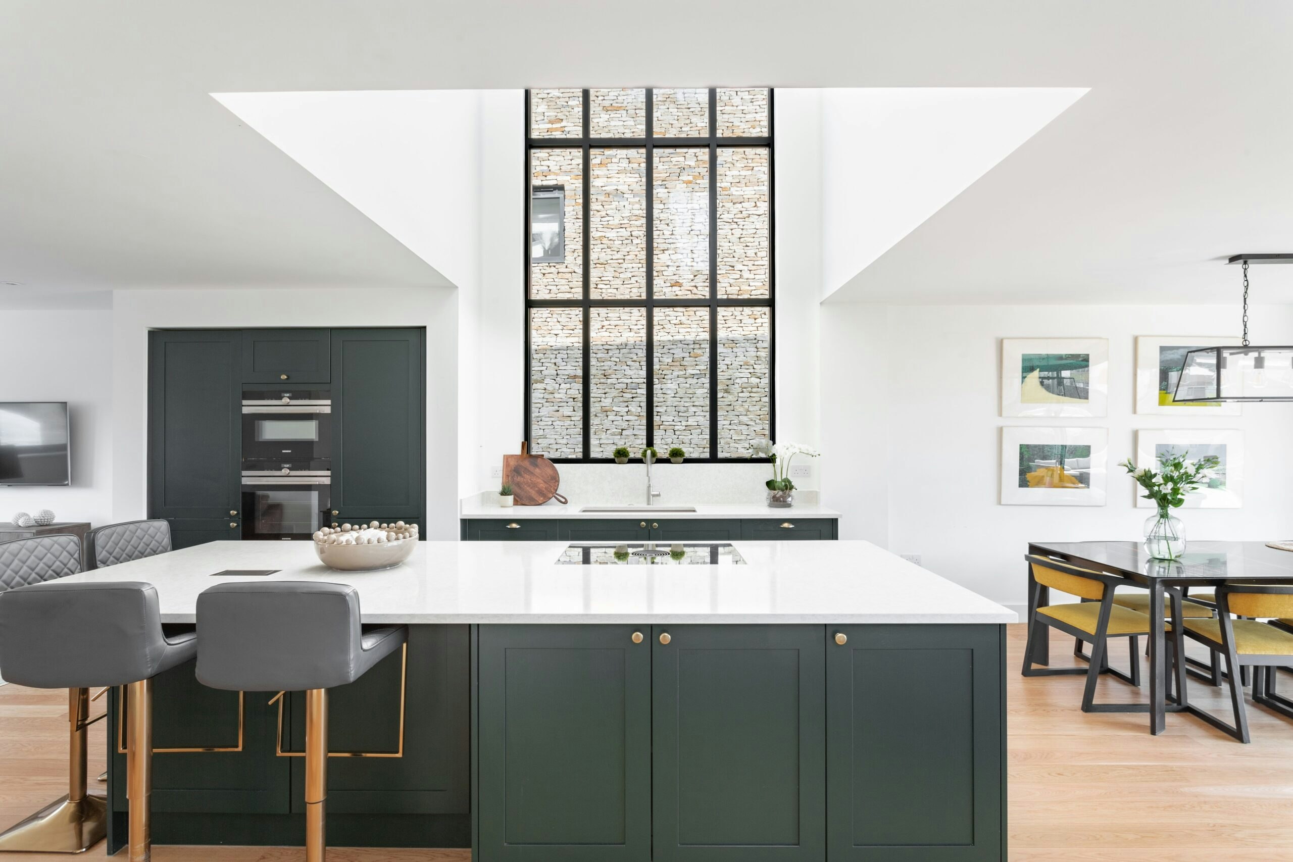 An inviting and homely kitchen in a rich Hunter Green colour. There is a cosy and luxury atmosphere. Sunlight filters in through large windows, illuminating the room with natural light.